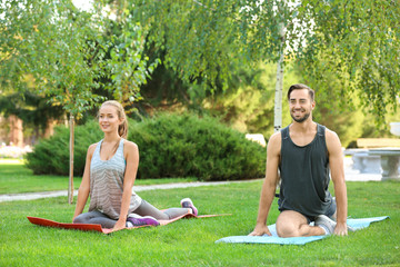 Young man and woman doing exercises on yoga mats in park