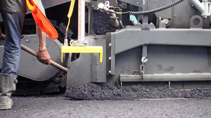 Road construction. Worker is applying new hot asphalt using road construction machinery and power industrial tools. Roadworks repaving process.