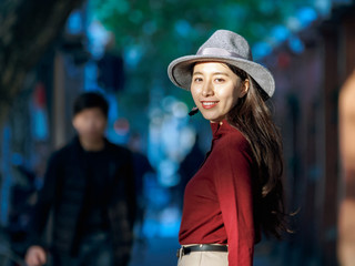 Pretty Chinese young woman stand in warm sunshine looking back in street.