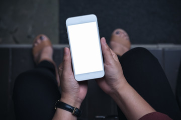 Top view mockup image of a woman sitting and holding white mobile phone with blank screen with concrete floor background
