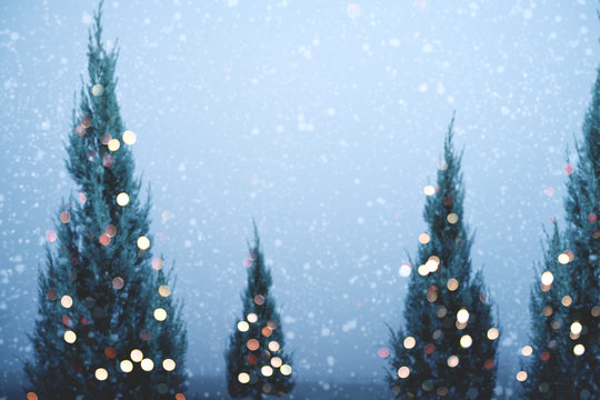 Blurred of Christmas tree and light bokeh with snowfall on sky background in winter. vintage color tone and rustic style.