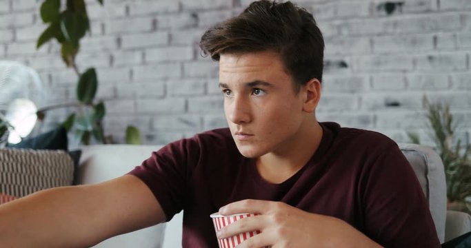 Close up face serious yong man sitting on the sofa watch tv eat popcorn at home bored casual freedom handsome laziness men remote Shot on RED EPIC camera Slow Motion Shot