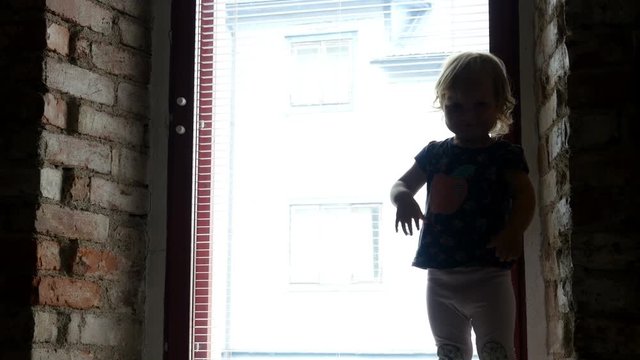 Kid Is Standing And Dancing By The Window At Home. Silhouette Of A Child On The Window