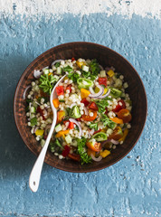 Israeli cous cous ptitim vegetables tabbouleh salad on a blue background, top view. Vegetarian food concept