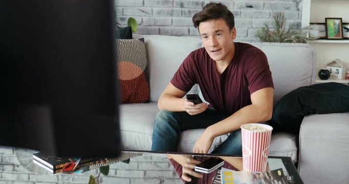 Happy man sitting on sofa watching television eating popcorn smiling at home modern design remote single time apartment couch looking men Shot on RED EPIC camera Slow Motion Shot