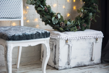 Christmas decorations with a spruce wreath on a chest and a chair against a brick wall background with garlands