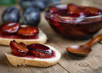 Bread slathered with plum jam with a wooden spoon on vintage table.