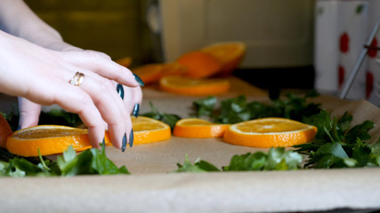 Female hands placing orange slices on baking tray tin in kitchen