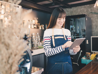 Young asian woman barista with a smile using tablet at bar counter, Owner small business concept.