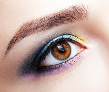 Closeup macro shot of human female eye. Girl with perfect skin and lilac - blue - yellow eyes shadows