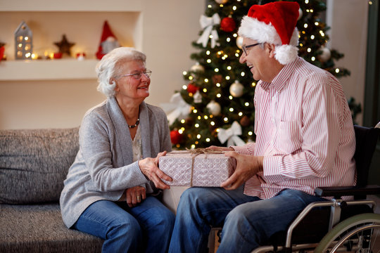 senior man in wheelchair and smiling woman with Christmas gift.