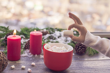 Christmas still life. Children's hands hold big marshmallows. A cocoa cup from marshmallows on a wooden table against the background of the New Year's still life. Selective focus