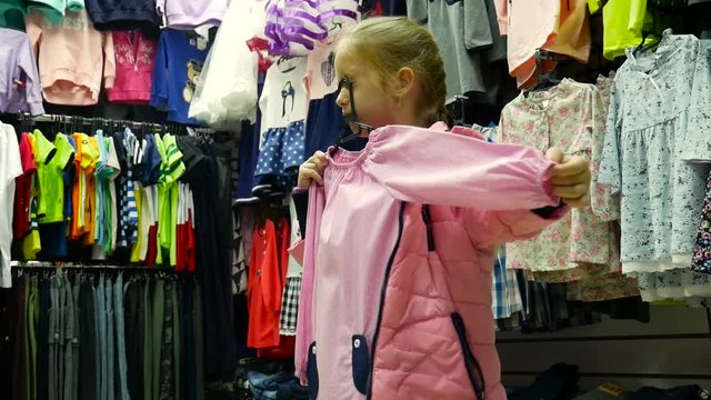 Little girl holding new dress in hands in children clothes boutique.