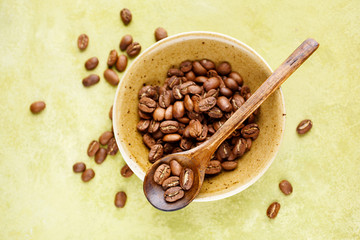 Fresh coffee beans in a bowl on a green background, top view. Selective focus,