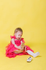 Girl toddler in a pink dress on a yellow background wearing the shoes on his feet