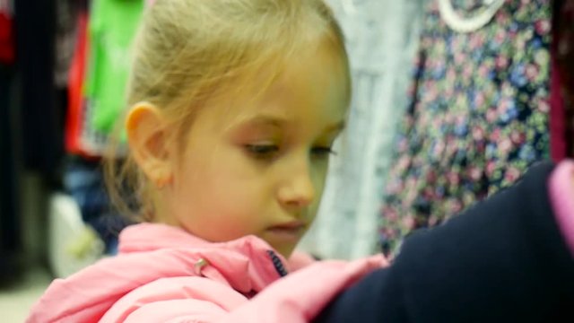 Little girl holding new dress in hands in children clothes boutique.
