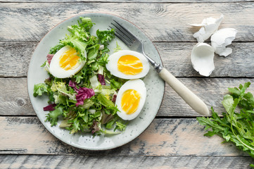 Vegetable salad with sliced boiled eggs and fresh lettuce and rucola served on wooden table. Top view. 