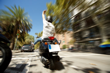 Rear view of man with helmet enjoying a fast scooter ride on city street