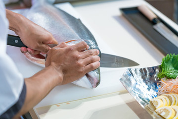 Japanese chef show preparing a fresh salmon with sharp knife on a cutting board  in...