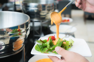 Tablespoon measure of creamy thousand island dressing being poured over fresh garden salad in breakfast buffet at hotel.