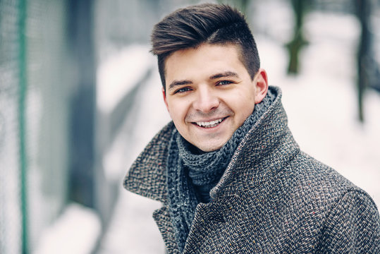 Close up portrait of handsome smiling young man in a warm coat walking dowm the street.