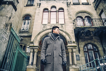 Portrait of stylish young man in warm grey coat and leather gloves on the background of old historic building.