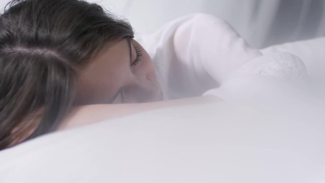Handheld shot of beautiful woman in white nightgown sleeping in bed, then waking up and looking around