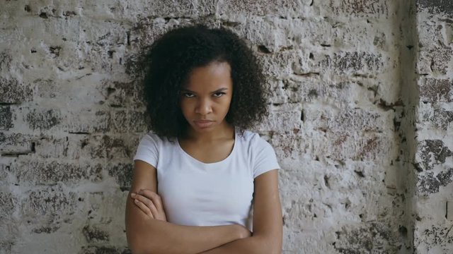 Portrait of angry curly mixed race woman looking into camera nervous on brick wall background