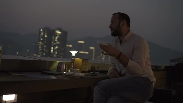 Young man relaxing and drinking cocktail sitting on terrace in bar at night 
