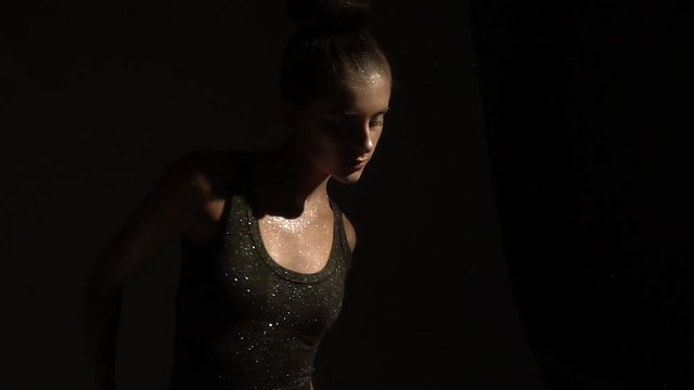 Beautiful teenage girl in sequins on body dances on a dark background