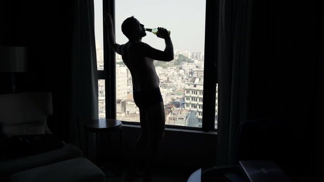 Silhouette of drunk man drinking wine standing by window at home
