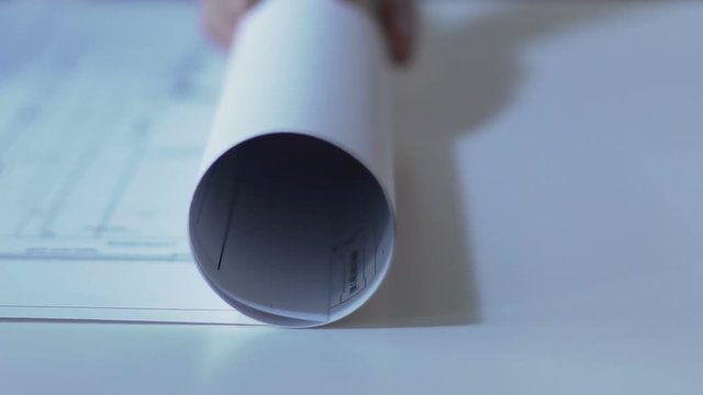 Designer unrolling building guidelines drawing on table, architecture design