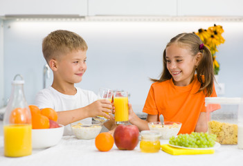 Happy siblings clink glasses with orange juice at breakfast