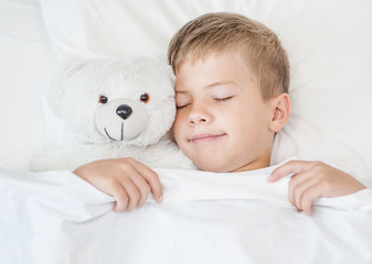 Little boy sleeping in bed with toy bear. Top view