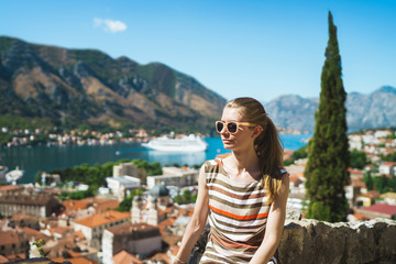 Fototapeta na wymiar Portrait of young tourist woman is sitting and looking at beautiful bay and mountains