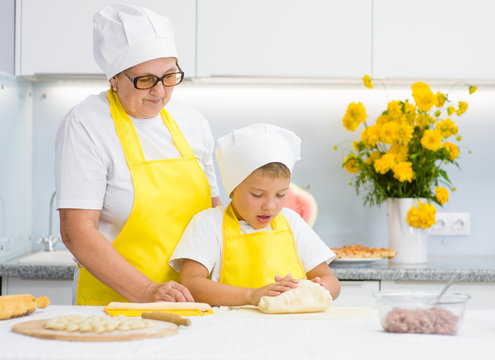 Happy grandmother teaches the child to knead the dough in the kitchen