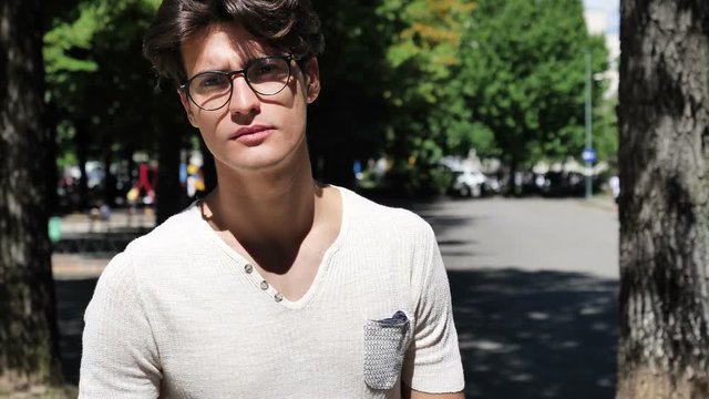Handsome but rude young man doing screw you sign with middle finger, outdoor in city park
