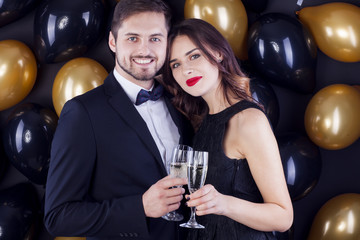 Elegant couple celebrate New Years Eve drinking champagne surrounded by black balloons.