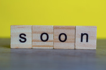 SOON word  on  wood cubes on table against yellow background