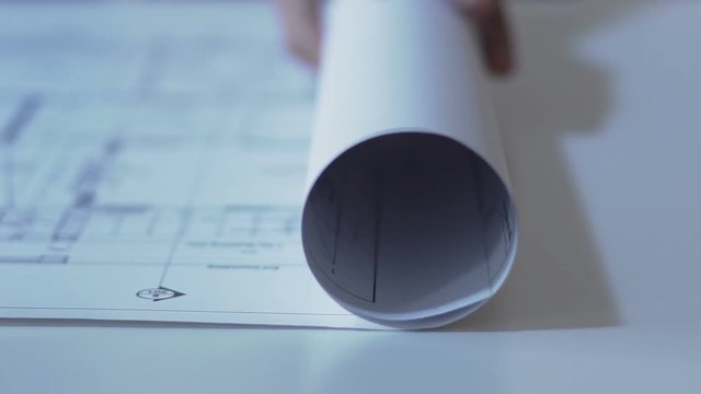 Designer opens drawing of building layout on paper, housing construction