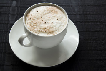 a white little cup of coffee with cream on the black wooden background