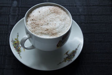 a white little cup of coffee with cream on the black wooden background