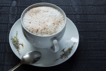 a white little cup of coffee with cream on the black wooden background