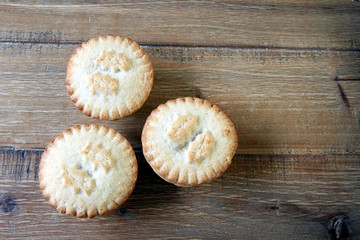 Overhead shot of three mince pies on a wooden table, a traditional Christmas dessert. Copy space for text