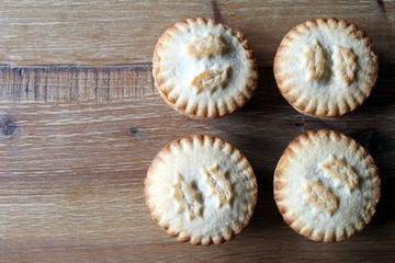 Overhead shot of four mince pies arranged neatly on a wooden table, a traditional Christmas dessert. Copy space for text