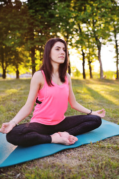 Young pretty girl sitting in lotus pose on green grass, practicing in yoga group. Healthy lifestyle