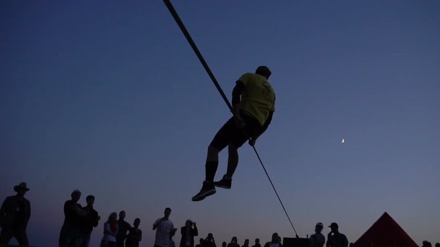 Athlete man jumping on The Rope and doing tricks at the twilights. Extreme sports festival. Slackline jumping
