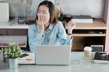 Young asian businesswoman yawning while working with laptop computer at office, woman in casual office lifestyle concept