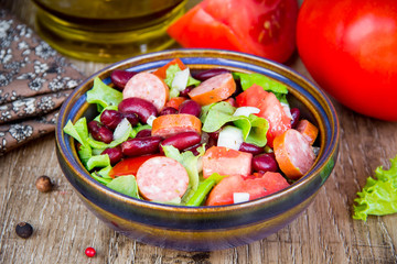 Salad with beans, tomatoes, onion, smoked sausage and lettuce, tasty dish in traditional rustic style