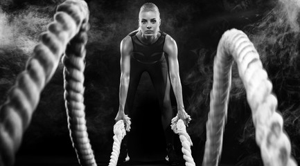 Fototapeta na wymiar Battle ropes session. Attractive young fit and toned sportswoman working out in functional training gym doing exercise with battle ropes. Fitness and workout motivation